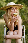 Young blonde woman eating apple sitting in green grass environment