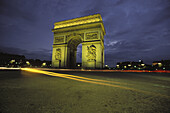 The Arc de Triomphe in Paris is located at the end of the Champs Elysees. This photo shows at night with car headlights as streaks of light. Paris. France.