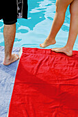 man/woman standing at edge of pool -woman dipping her foot in water