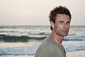 Horizontal shot of a good-looking man in a green t-shirt next to the Indian ocean with the sun setting.