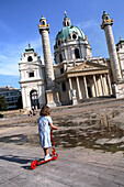 Mädchen mit Roller auf Karlsplatz mit Karlskirche im Hintergrund, Wien, Österreich