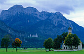 Europa, Deutschland, Bayern, Schwangau bei Füssen,  Wallfahrtskirche St. Coloman umgeben von Bäumen und Schloss Neuschwanstein in den Bergen