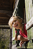 Girl looking out of a window of a wooden hut, Austria