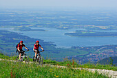 couple mountainbiking near Steinlingalm with view to lake Chiemsee, Kampenwand, Chiemgau range, Bavarian range, Chiemgau, Upper Bavaria, Bavaria, Germany