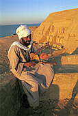 Bearded man playing sithar at the sunrise, Abou Simbel Ramasses temple at back. Nubia . Egypt.