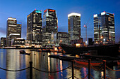 Canary wharf financial district showing skyscraper towers at night dusk evening overlooking water with reflections and ships docked in water isle of dogs. London. England. UK