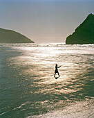 Woman walking in the shallow water at Wharariki Beach, northwest coast, South Island, New Zealand