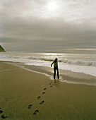 Woman walking on the beach under clouded sky, West coast, South Island, New Zealand