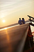 Couple sitting on a jetty, Ambach, Lake Starnberg, Bavaria, Germany