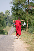 Young burmese monk carrying water tnks over his shoulders near Mount Popa, Myanmar, Burma