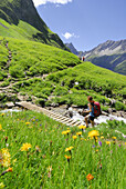 Woman crossing a creek on the way to alpine lodge Memminger hut, Lechtal range, Tyrol, Austria