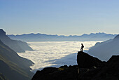 Hiker standing on crag above fog bank in valley Gschnitz, Stubai Alps, Stubai, Tyrol, Austria
