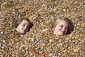 Children buried on pebbly beach, Brighton, England, UK