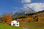 Typical house in Engadin with trees in autumn colours and view to Piz Lischana and Piz San Jon, Tarasp, Unterengadin, Engadin, Grisons, Switzerland