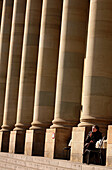 Woman sitting between the columns of the Koenigsbau in the sunlight, Stuttgart, Baden-Wuerttemberg, Germany