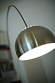 Moderne angeknipste Stehlampe mit einem glänzenden, runden und chromfarbenen Lampenschirm