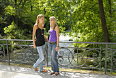 Two young women standing on a bridge crossing Isar channel, Englisch Garden, Munich, Bavaria, Germany