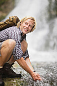 Junger Mann trinkt an einem Wasserfall, Werdenfelser Land, Bayern, Deutschland