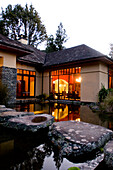 View over a pond at the illuminated windows at the Treetops Lodge in the evening, North Island, New Zealand, Oceania