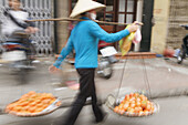 Woman street vendor carrying yoke baskets, Hanoi, Vietnam