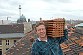 portrait, roof tiler carrying tiles on shoulder, on roof, Berlin skyline in background, Berlin, Germany