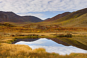 Clouds and mountains reflected in small tundra lake of the Ogilvie Mountains, Tombstone Territorial Park, Yukon, Canada