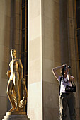 A visitor taking photo beisde a gilded bronze statue in the central square of the Palais de Chaillot. Paris. France