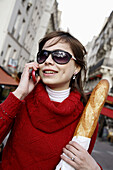 A young woman holding a baguette and talking on her cell phone on the street of Paris. Paris. France.