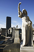 A tomb statue in Cimetiere du Montparnasse with the high-rise Tour Montparnasse in the background. Paris. France