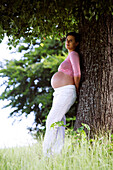 Pregnant woman leaning against a tree