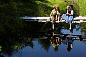 Boy and girl in traditional dress sitting on a wooden jetty at a lake, Alp, South Tyrol, Italy