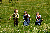 Girl and boy wearing traditional clothes running through an Alpine meadow, Farm holidays, Agriculture, South Tyrol, Italy