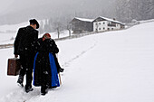 Farmer and mother walking through the snow towards farmhouse, Agriculture, South Tyrol, Italy