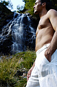 Man with naked upper body in front of a waterfall in the sunlight, Schnals valley, Val Venosta, South Tyrol, Italy, Europe