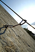 View over a climbing rope at a rock face to a lake in the sunlight, South Tyrol, Italy, Europe