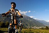 Junges Paar auf Mountainbikes unter blauem Himmel, Vinschgau, Südtirol, Italien, Europa