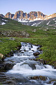 Alpenglow on peaks above American Basin with an unnamed creek rushing through green meadows, San Juan Mountains, Colorado, USA