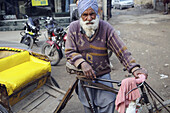 A Sikh cycle rickshaw driver standing by his rickshaw in the noisy streets of Amritsar, India