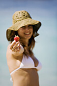 Woman holding a strawberry on the beach