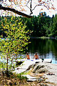 Menschen sitzen auf einem Holzsteg im Sonnenlicht, Saimaa Seenplatte, Finnland, Europa