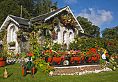 Small cottage near Luss at Loch Lomond, Scotland, United Kingdom, with the garden decorated with garden gnomes, ornaments, wooden dolls, manakins and a train with carriages made from wooden barrels