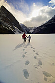 A father and son walking on Lake Louise with the Chateau Lake Louise Hotel in the background, Banff National Park, Alberta, Canada