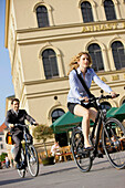 Two businesspeople riding bicycles at Odeonsplatz, Munich, Bavaria, Germany