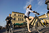 Two businesspeople riding bicycles at Odeonsplatz, Munich, Bavaria, Germany