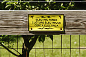 Electric fence sign on wood-and-wire fence, tree and grass behind, south central Indiana, USA