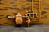 Natural gas meter with pipes running through valves and apparatus against a yellow brick wall