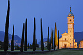 Illuminated church San Abbondino near Gentilino with cypress alley, Gentilino, Lugano, Ticino, Switzerland