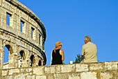 Paar auf der Stadtmauer vor dem römischen Amphitheater unter blauem Himmel, Pula, Kroatische Adriaküste, Istrien, Kroatien, Europa
