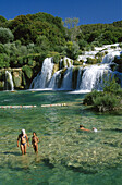 Menschen baden an den Krka Wasserfällen unter blauem Himmel, Krka Nationalpark bei Sibenik, Kroatische Adriaküste, Dalmatien, Kroatien, Europa