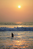 Bathing man at sunset, Lighthouse beach, Kerala, India